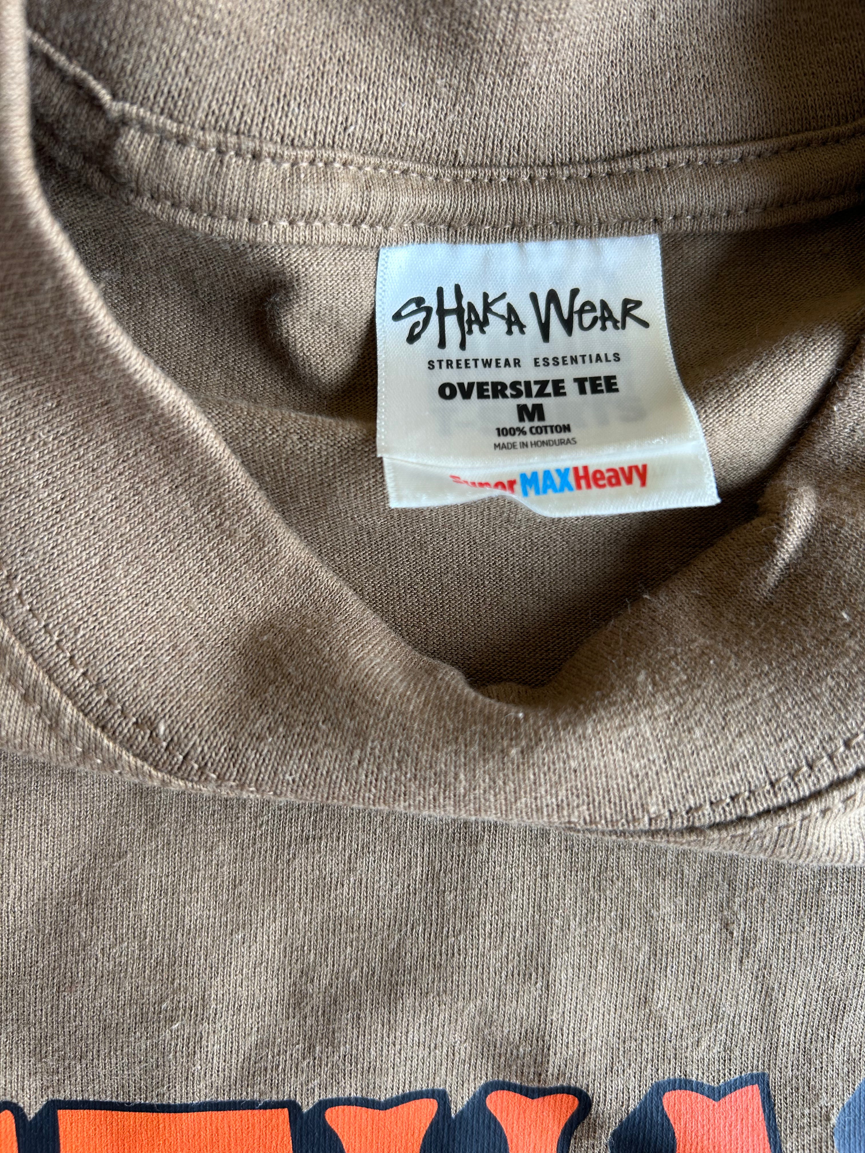 Close-up of the inside collar of a taupe-brown oversized t-shirt, showing the white 'SHIWA WEAR' brand label.