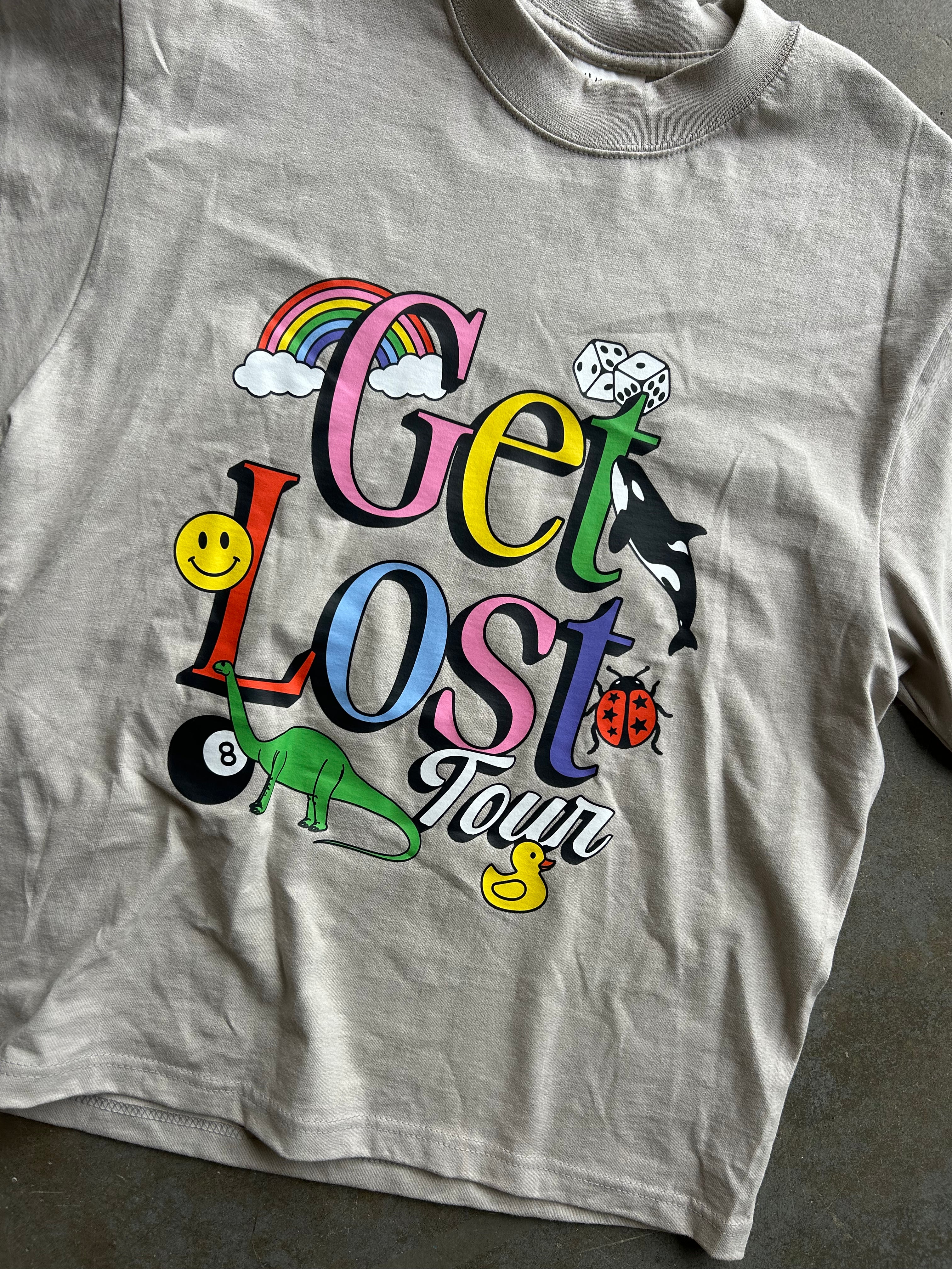 A light gray crewneck t-shirt featuring a colorful graphic print on the front with the words 'Get Lost Your' in stylized letters, accompanied by cartoon illustrations including a rainbow, smiley face, duck, ladybug, dinosaur, and orca.