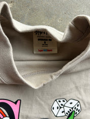 Close-up of the inside collar of a beige crewneck sweatshirt, showing the inner label with 'STUSSY' and 'OVERSIZE FIT', along with 'Super MAX Heavy' text, laid flat on a gray concrete surface.