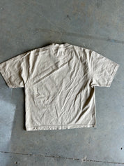 A light beige short-sleeve t-shirt laid flat on a gray concrete floor.