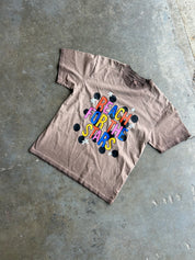 A faded brown short-sleeve t-shirt with a colorful retro graphic reading 'REACH FOR THE STARS' in rainbow letters with black and white stars, laid flat on a concrete floor.