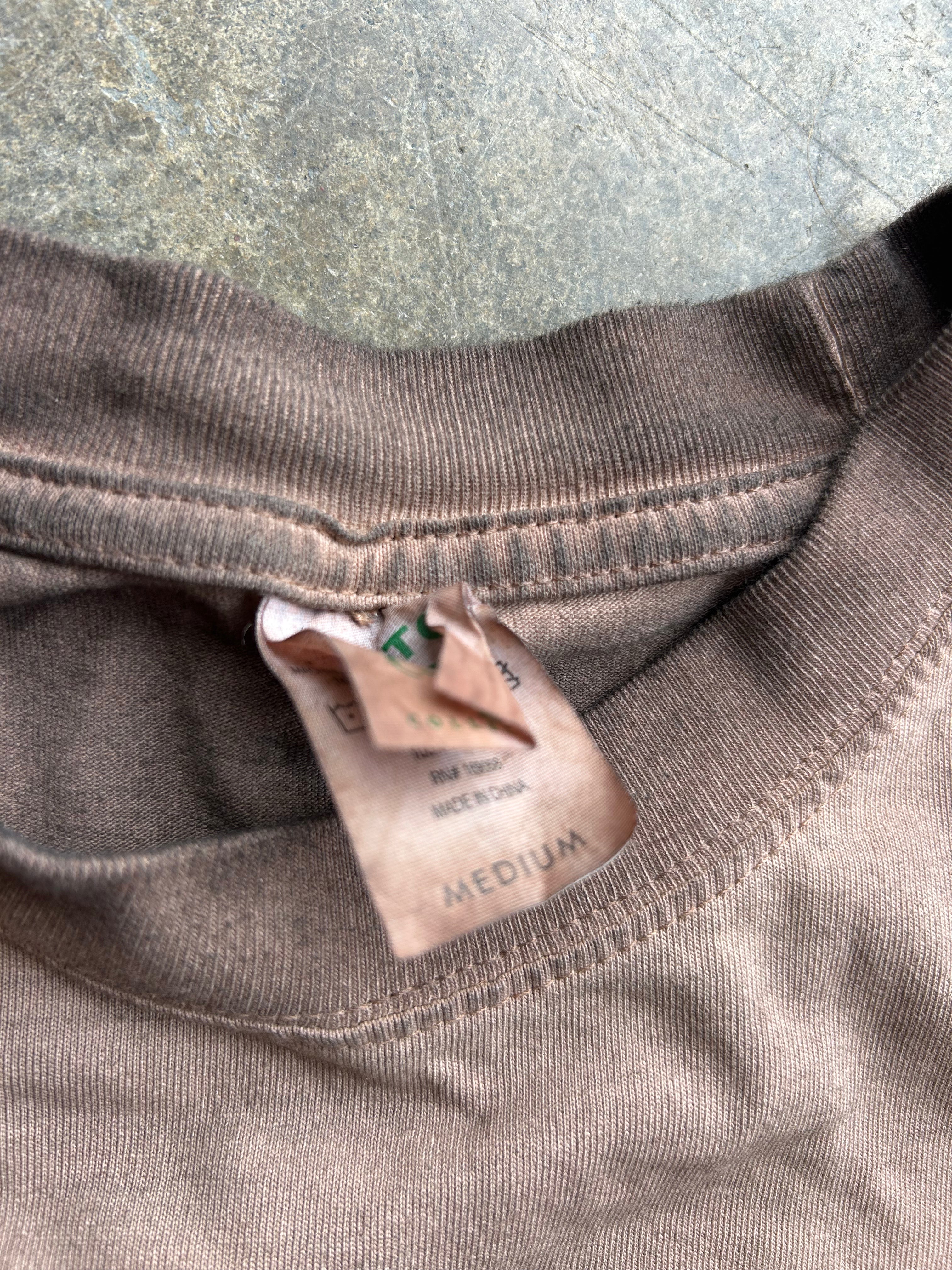 Close-up of a brown ribbed knit garment neck with a torn paper size tag reading MEDIUM, placed against a textured gray surface.