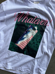 A white graphic t-shirt laid flat on a dark surface. The shirt features a large rectangular print of an astronaut floating on a pink float in green water, with the word 'Whatever!' written in pink script above the graphic.