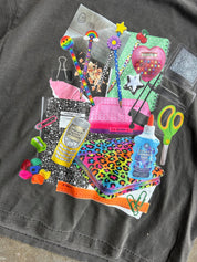 A collage of colorful school supplies and stationery items arranged on a dark gray fabric background, including notebooks, pens, scissors, paper clips, a glue bottle, a phone-shaped item, and other bright stationery accessories.