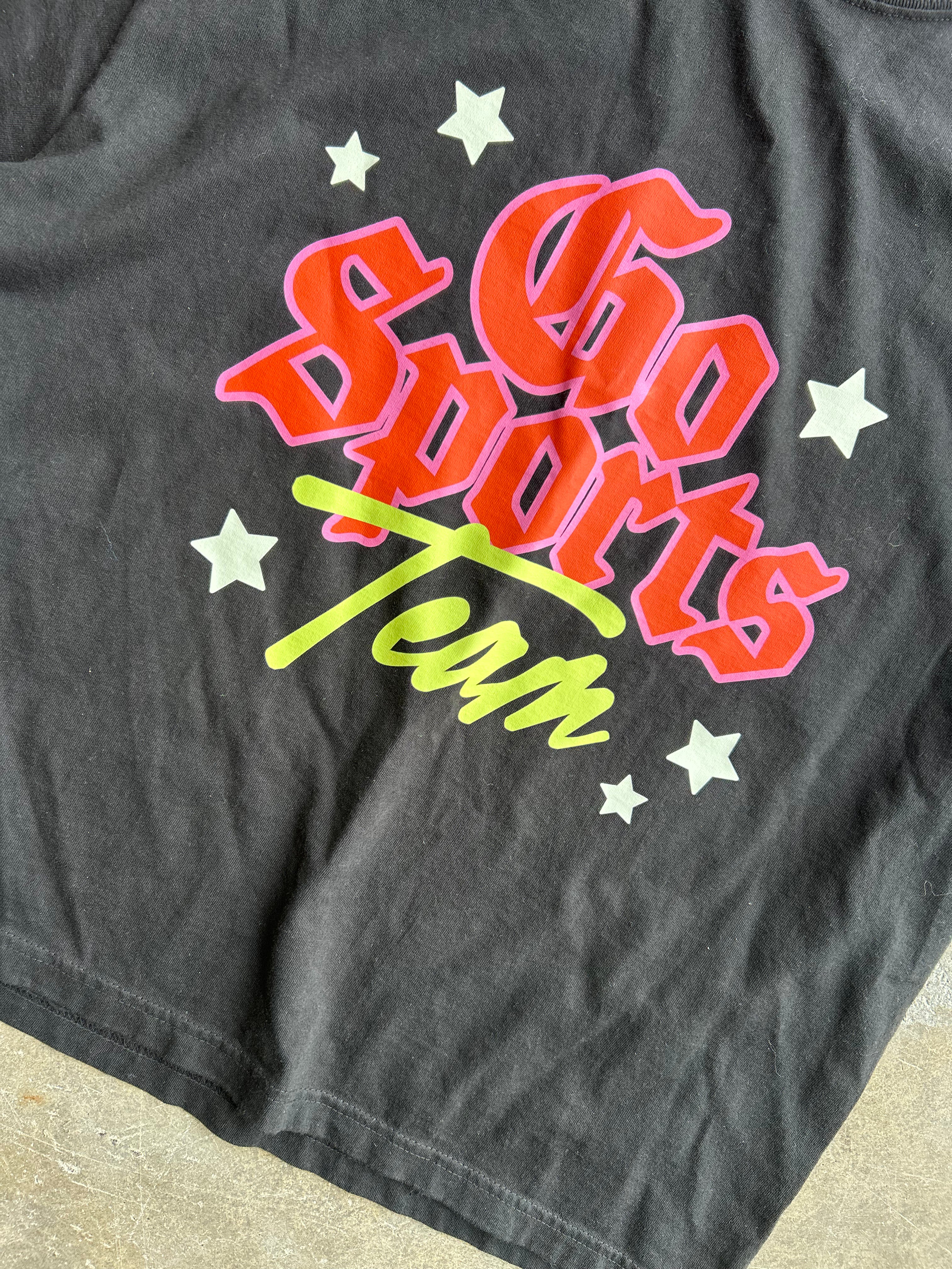 A close-up of a dark gray t-shirt featuring a colorful graphic that reads 'Go Sports Team' in red, pink, and green retro lettering, surrounded by white stars.