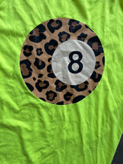 A close-up of a bright neon green fabric surface featuring a large circular graphic of a leopard-print 8-ball pool icon with the number 8 in black.