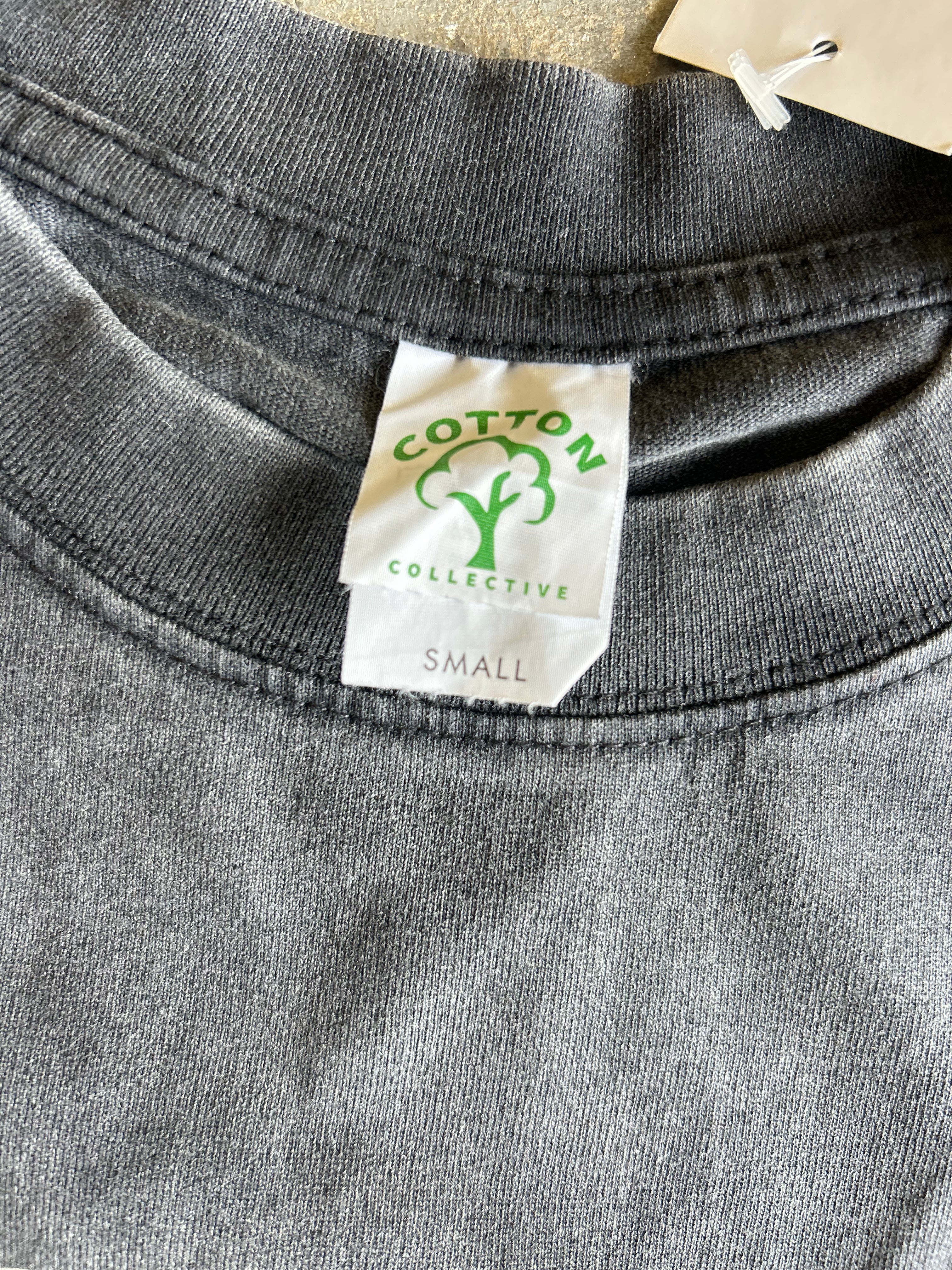 Close-up of a dark gray heather crewneck t-shirt showing the inner neck label which reads 'COTTON COLLECTIVE' with a green tree logo and 'SMALL' printed below.