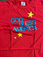 A red short-sleeve t-shirt with 'GOD BLESS AMERICA' printed in blue outline letters and three yellow stars, laid flat.