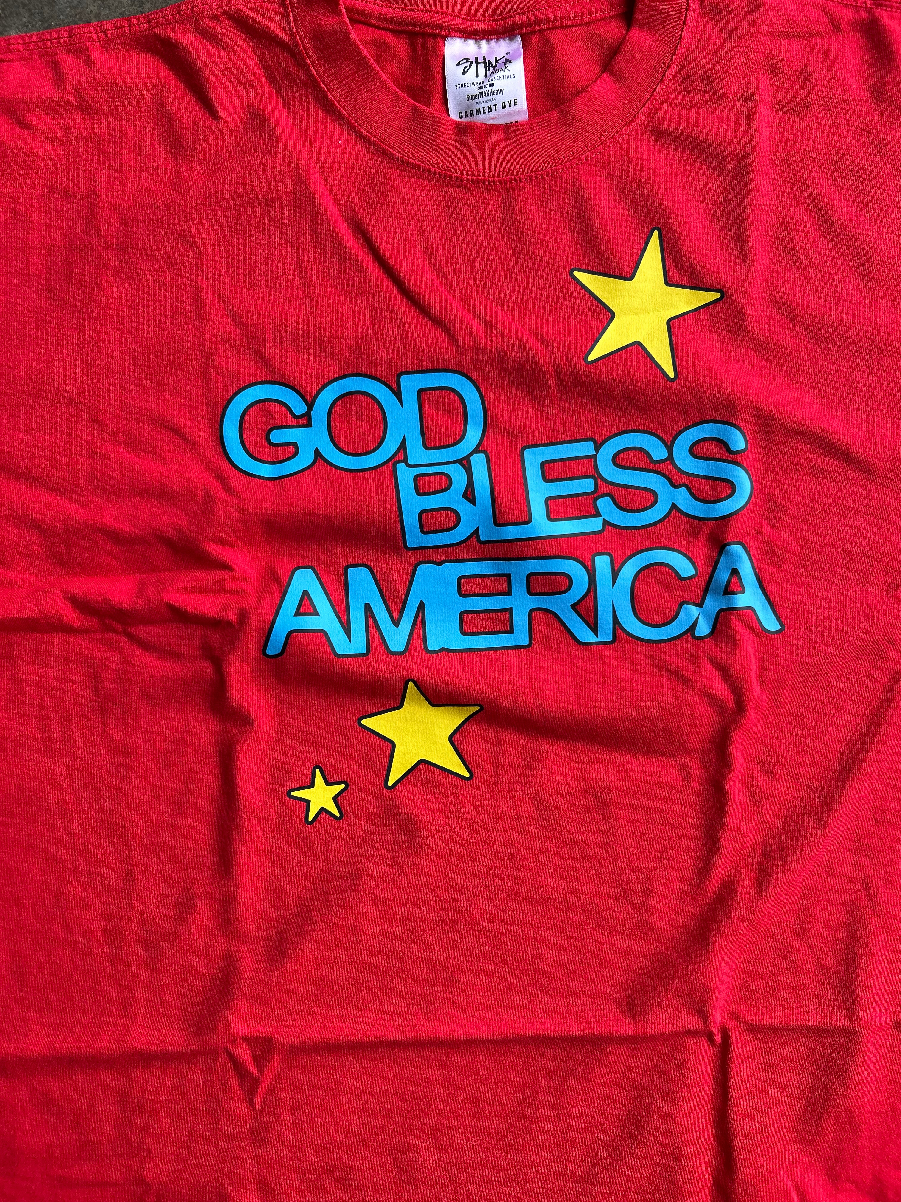 A red short-sleeve t-shirt with 'GOD BLESS AMERICA' printed in blue outline letters and three yellow stars, laid flat.