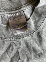 Close-up of a gray heather crewneck sweatshirt showing the inner neck label which reads 'SHAKA WEAR' and 'DROP SHOULDER GARMENT SWEATSHIRT' with size 'M'.