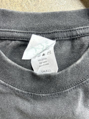 Close-up of the inside collar of a dark gray t-shirt, showing a white paper care tag with size and material information.