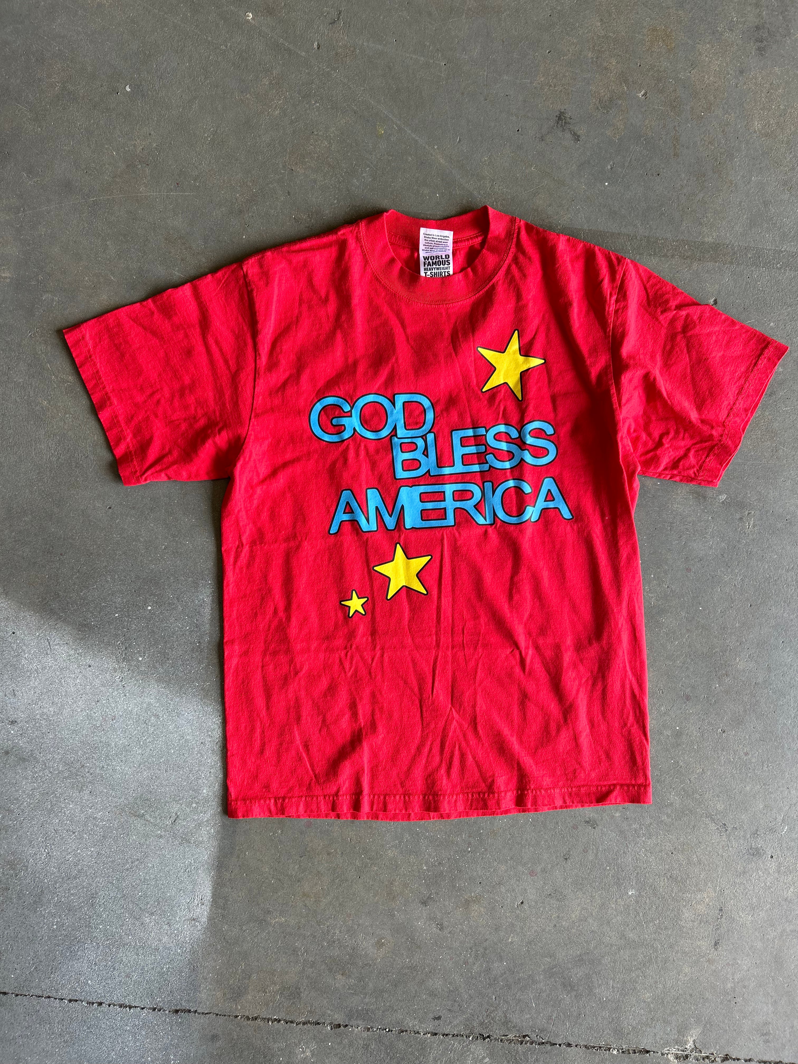 Red tee with God Bless America text and yellow stars on a concrete surface. 