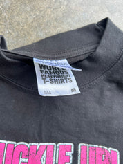 Close-up of the inside collar of a black heavyweight T-shirt, showing the white woven neck label that reads 'WORLD FAMOUS HEAVYWEIGHT T-Shirts' and 'M'. Part of a bright pink graphic print is visible at the bottom.