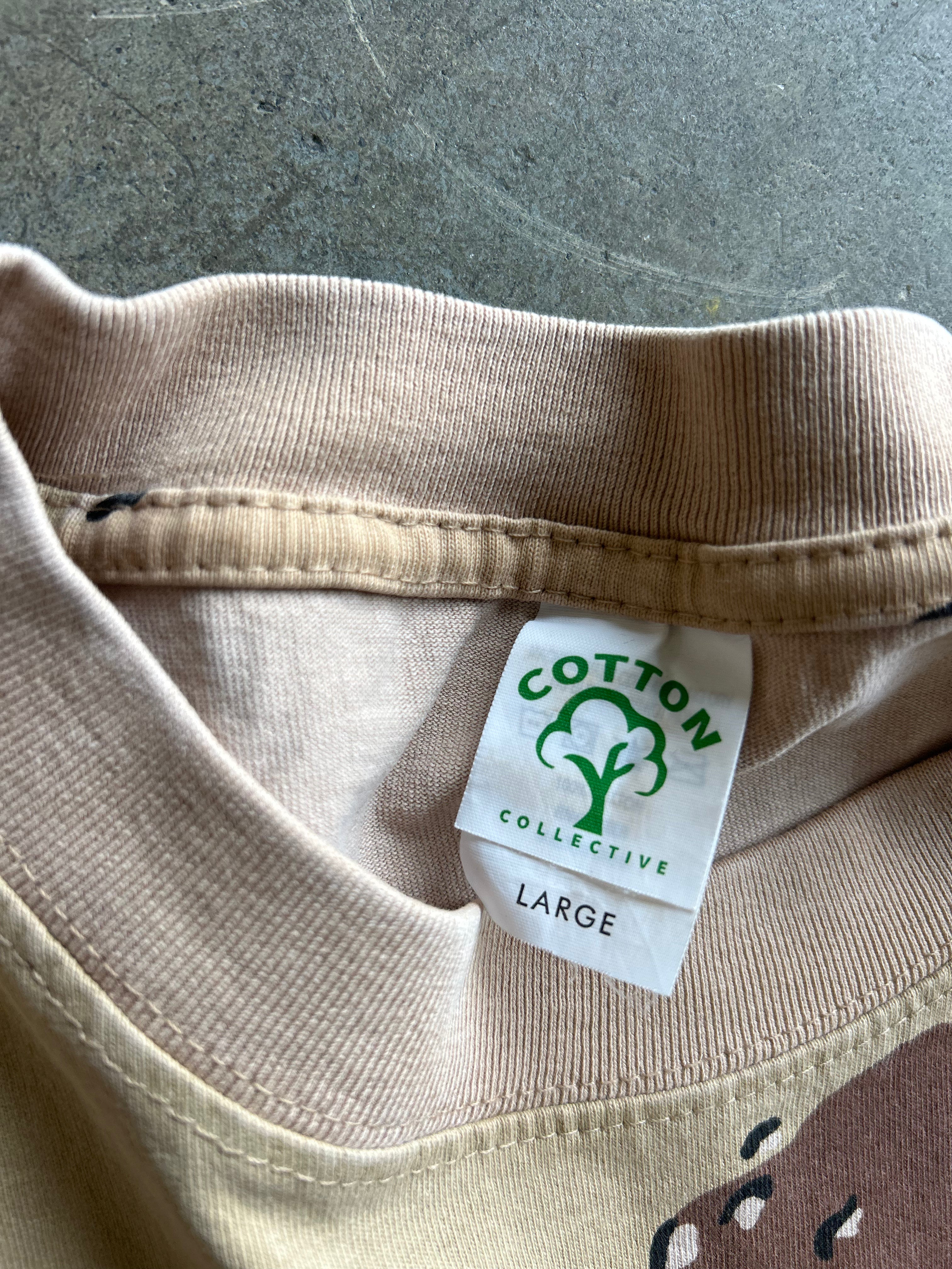 Close-up of a beige ribbed knit garment collar with a sewn-on white label reading COTTON COLLECTIVE and LARGE, photographed against a gray concrete-like surface.