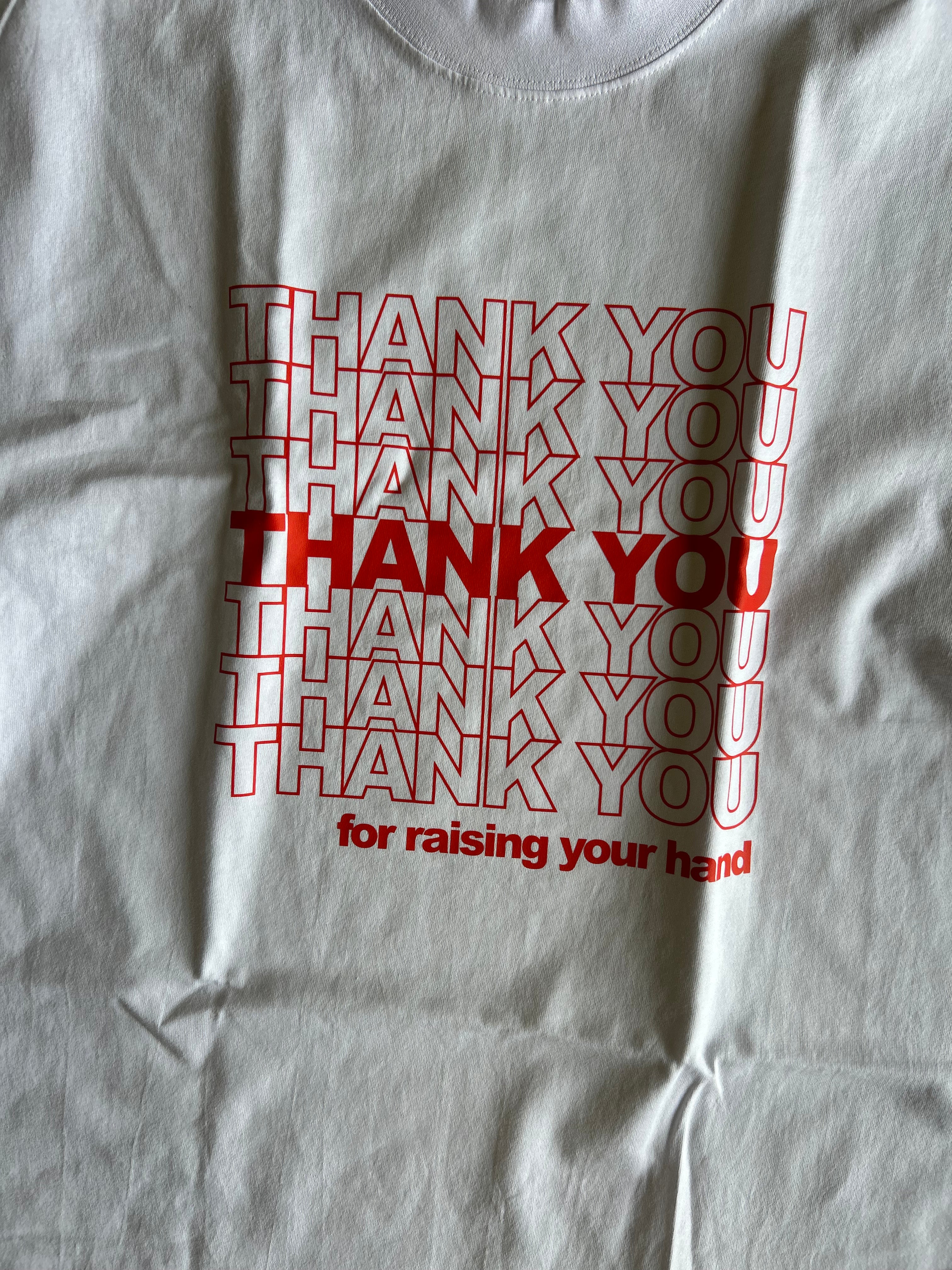 A close-up of a white t-shirt featuring a red graphic print that reads 'THANK YOU for raising your hand' in a layered, repeating style.