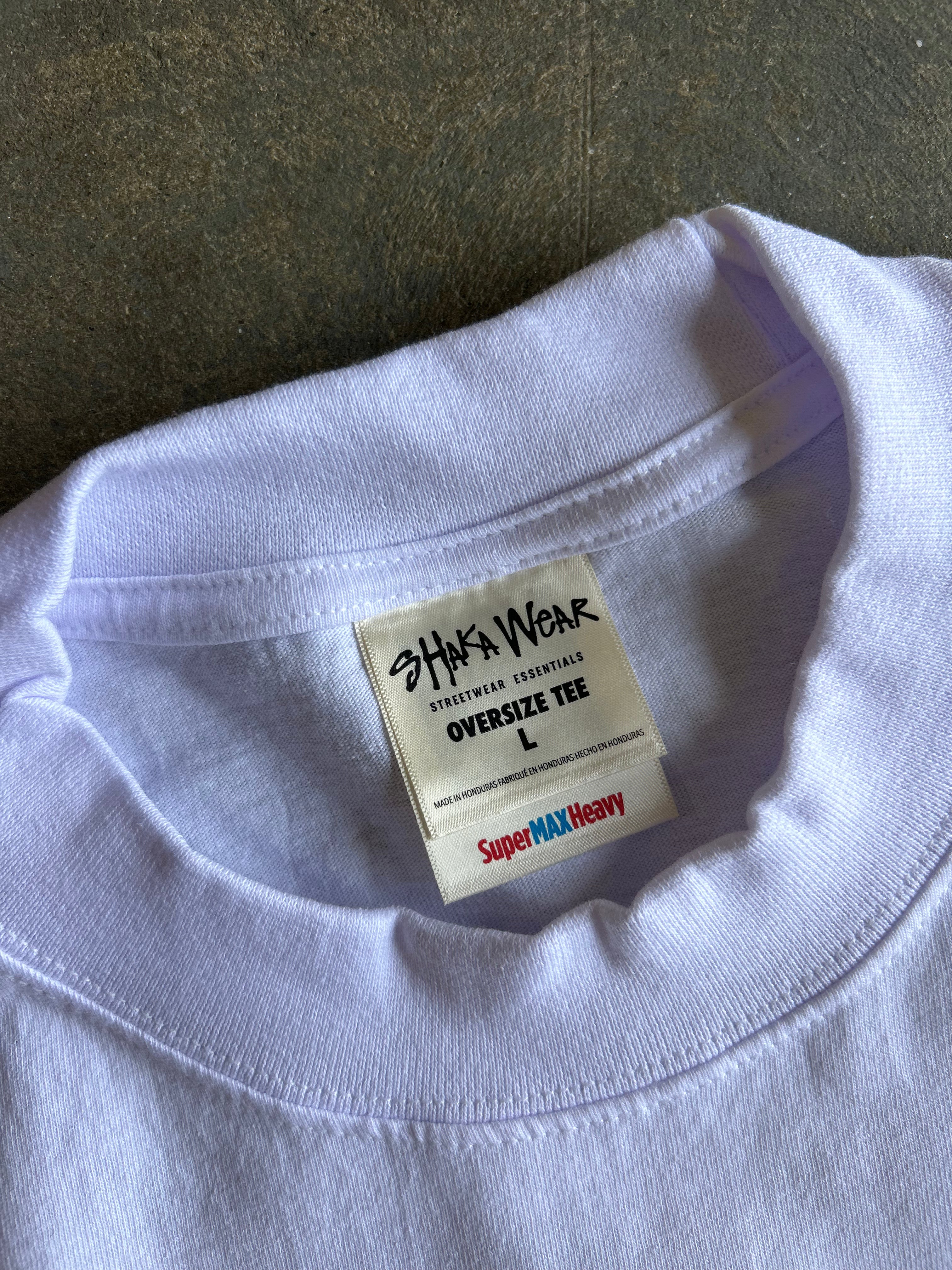 Close-up of a light lavender-purple crewneck t-shirt collar, showing a white inner neck label that reads 'SHAKA WEAR' and 'SUPER MAX HEAVY'.
