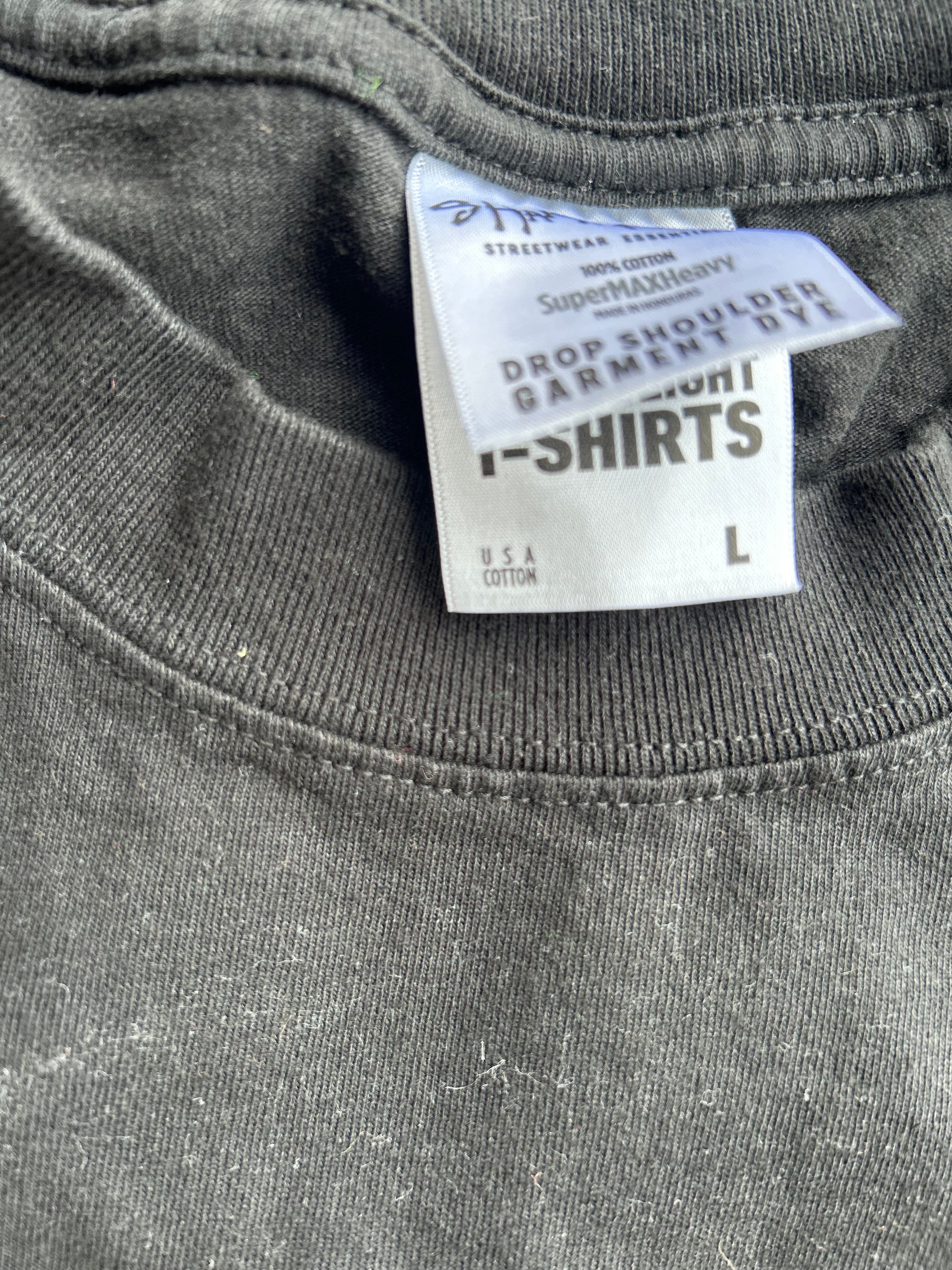 Close-up of a dark gray t-shirt neck collar showing the inner care label which reads 'Streetwear Selection' and 'Drop Shoulder Garment Dye'.