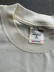 Close-up of a cream-colored oversized cotton t-shirt collar, showing the inner neck label for 'Shaka Wear' and 'SuperMAX Heavy' weight.