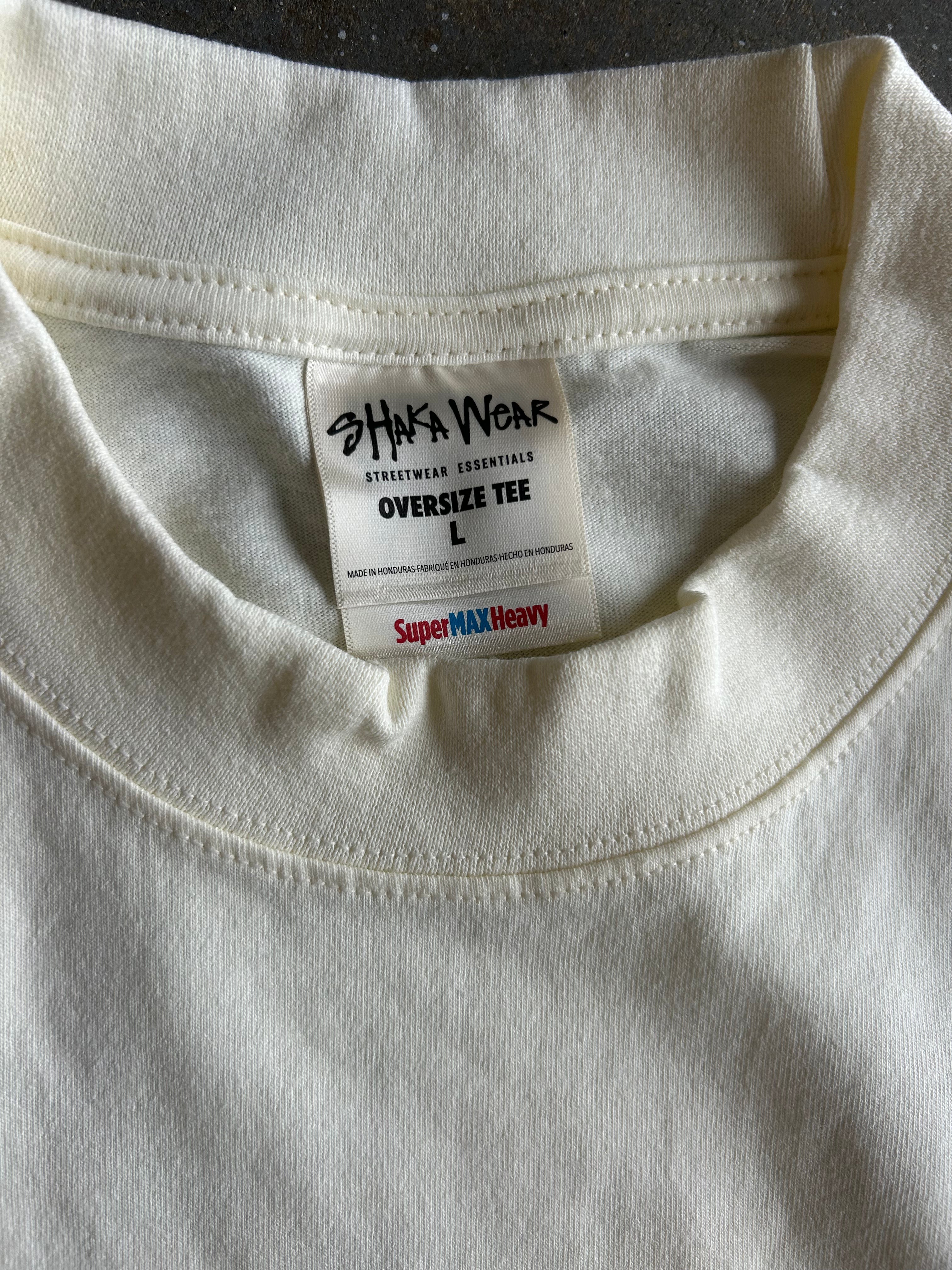 Close-up of the inside collar of an off-white/cream oversized t-shirt, showing the inner label for 'Shaka Wear' and 'SuperMAX Heavy'.