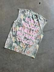 A sleeveless tank top with a woodland camouflage pattern and pink text reading 'BUILT TOUGH FUELED BY PURE CHAOS', laid flat on a gray concrete floor.