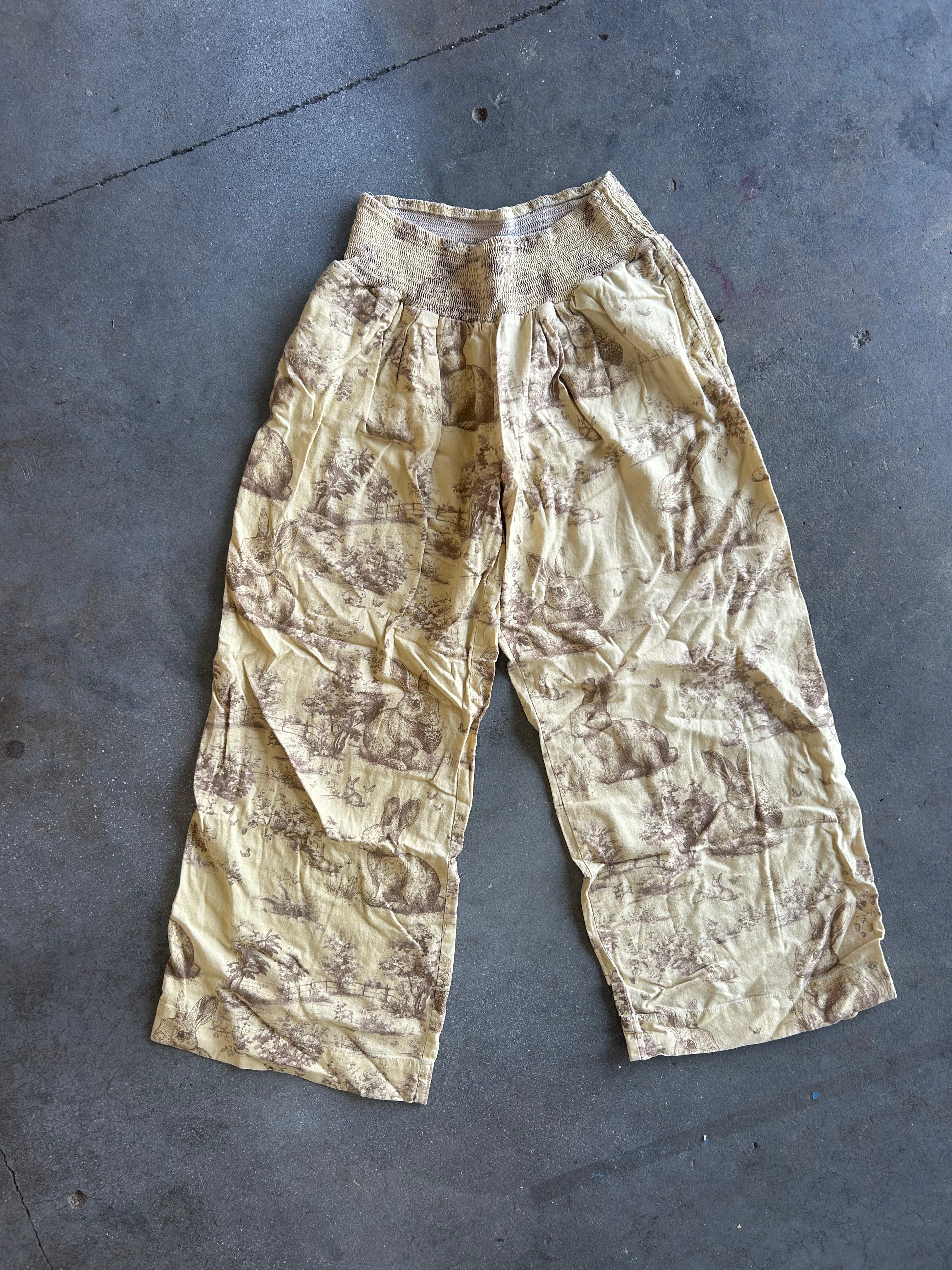 Cream linen pants with brown designs on a concrete backround