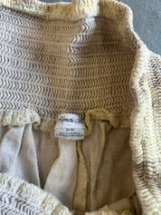 Close-up of a beige and cream textured knit garment, showing a white fabric brand label that reads  'M'