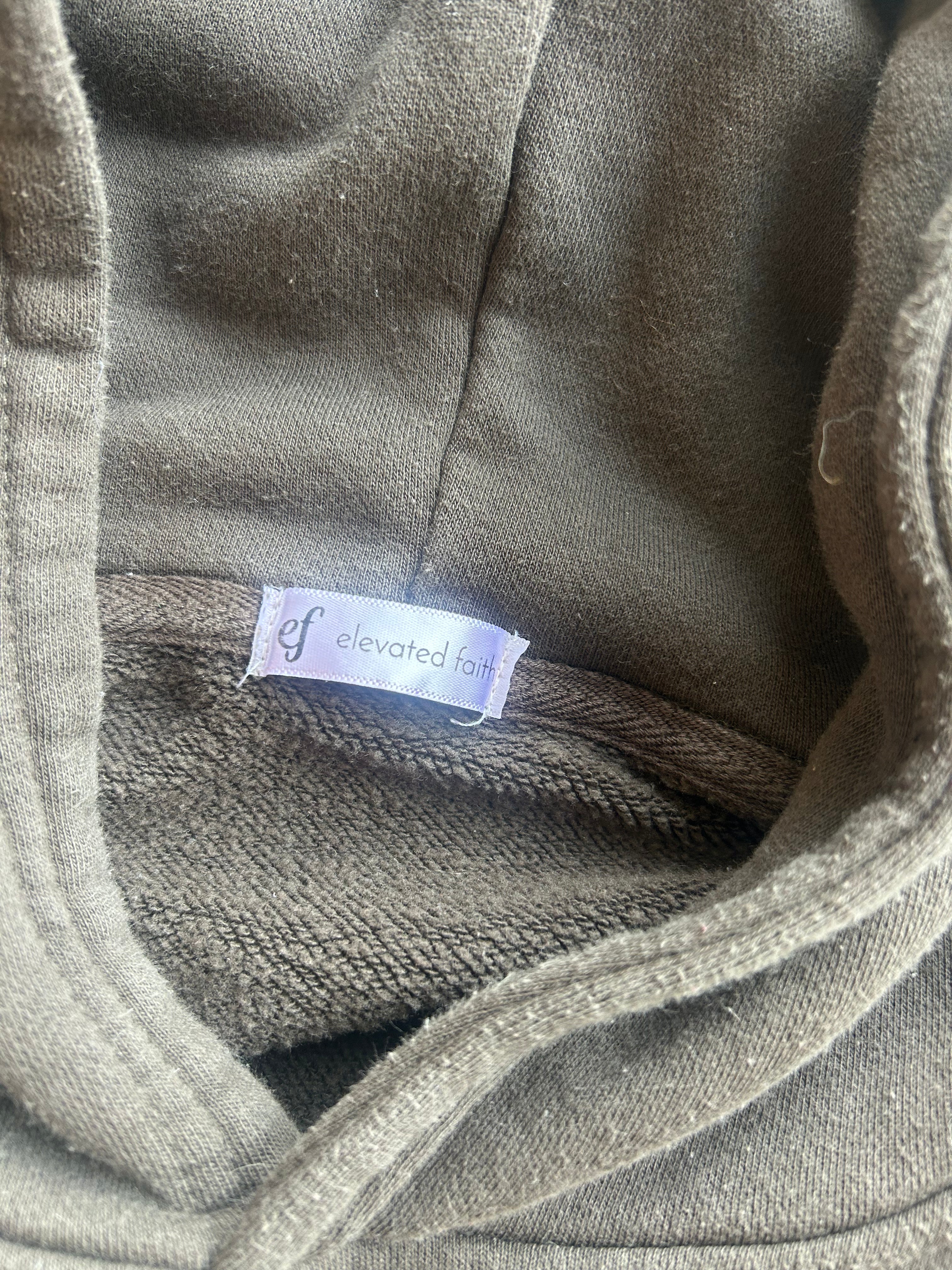 Close-up of a hooded garment in a muted taupe-gray color, showing the interior lining and a small sewn-in label that reads 'elevated fashion'