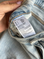 Close-up of a light-wash blue denim garment, showing the inside waistband and a white American Eagle size tag held by a hand