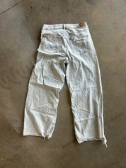 A pair of light-wash, faded blue jeans laid flat on a concrete floor, viewed from the back