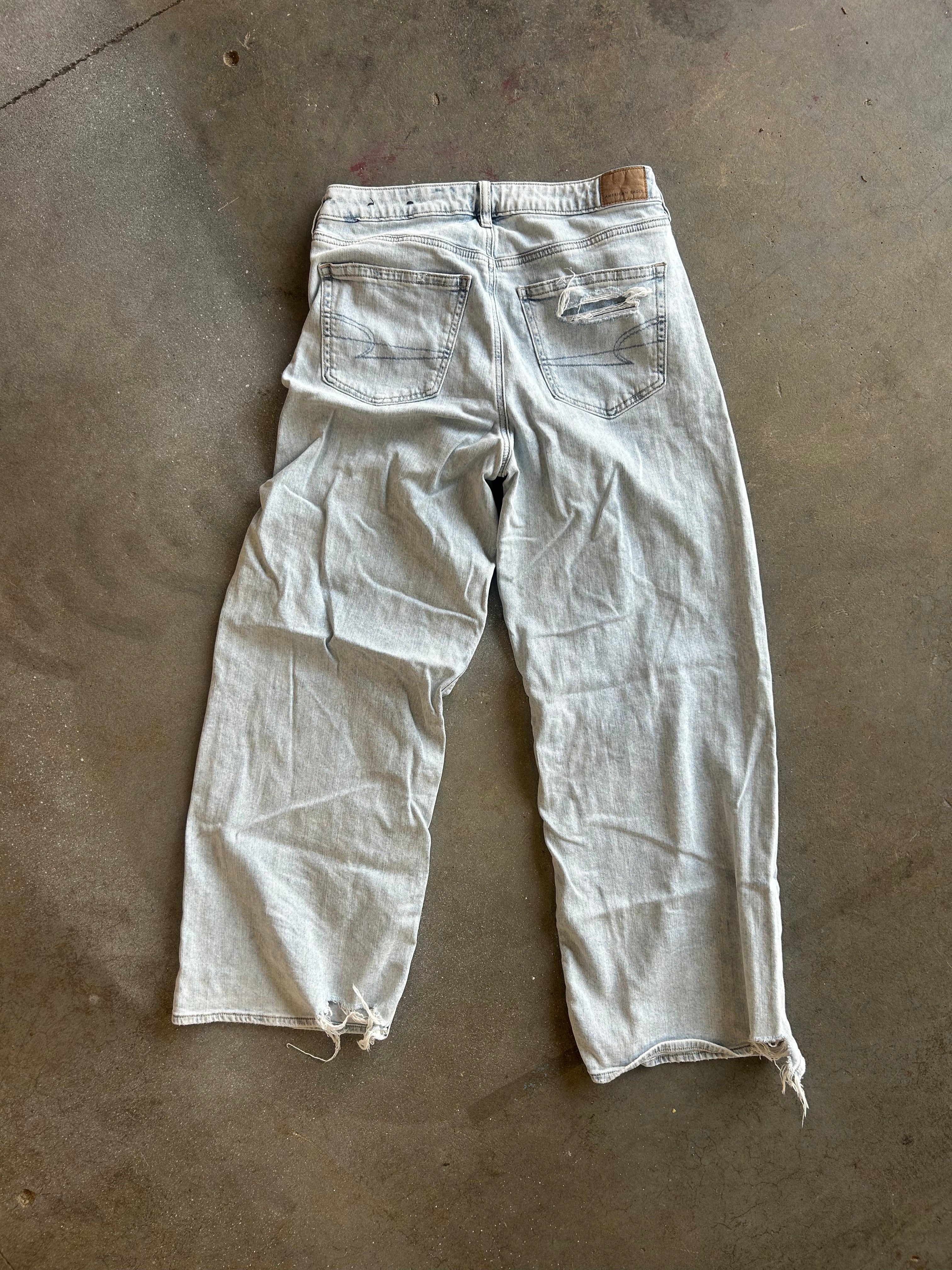 A pair of light-wash, faded blue jeans laid flat on a concrete floor, viewed from the back