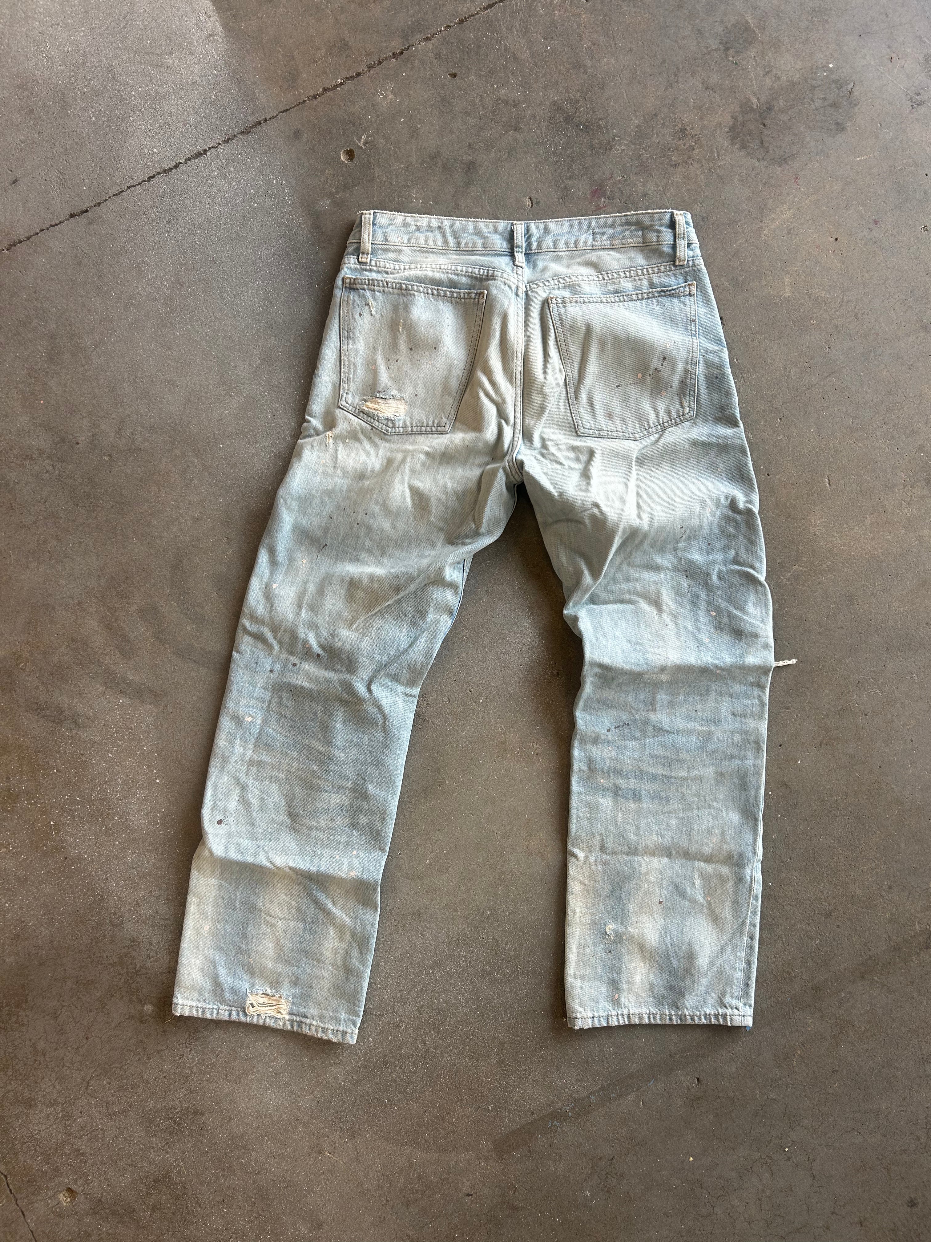 Light-wash distressed denim jeans laid flat on a concrete floor, viewed from the back