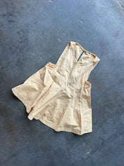 A sleeveless, scoop-neck beige linen dress or tunic laid flat on a textured dark gray concrete surface