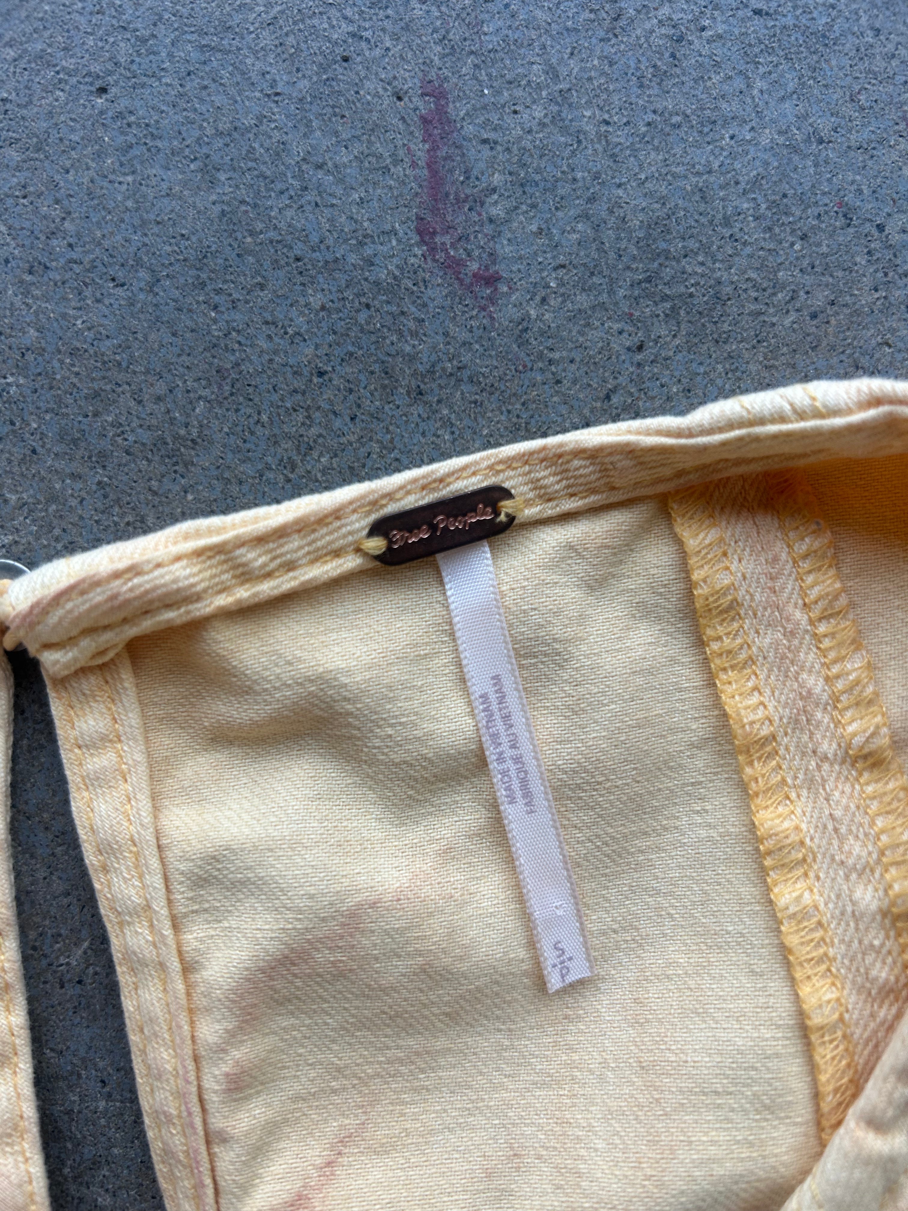 A close-up of a cream-colored woven textile, likely a sarong or scarf, featuring a small brown brand label reading 'Breezeflow' and a white size tag, laid flat on a gray concrete surface