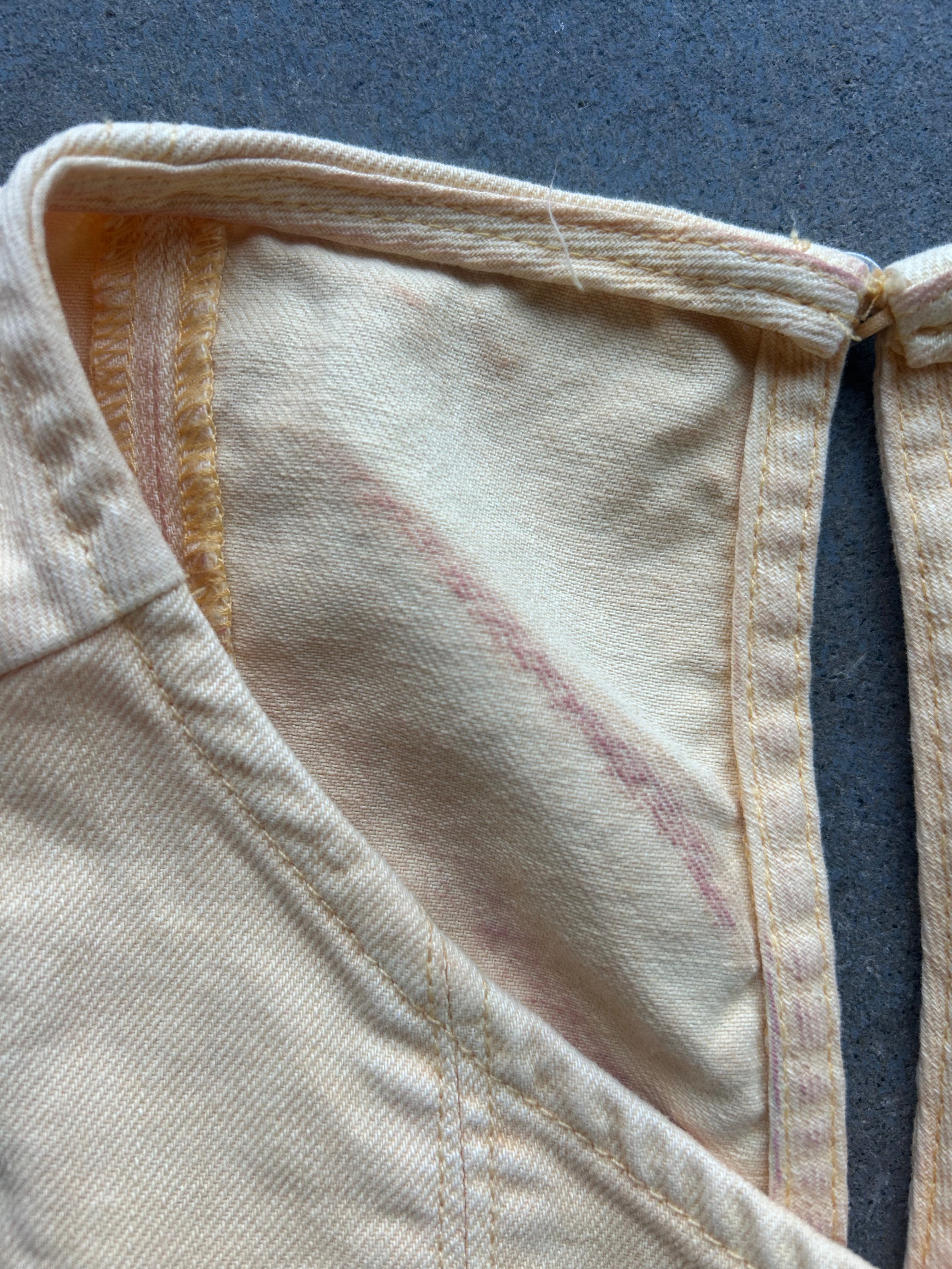 Close-up of a cream-colored garment with visible pinkish-red stained areas on the inner fabric, showing the texture of the textile and stitching