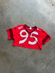 A red Nike football jersey with the number 95 in white on the front, laid flat on a gray concrete floor