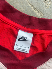 Close-up of a Nike athletic jersey neck label on red mesh fabric, with a gray concrete-like surface visible in the background