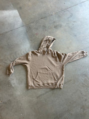 A light brown hooded sweatshirt laid flat on a gray concrete floor