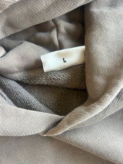 Close-up of a taupe-beige knit garment with a white size tag marked with the letter L