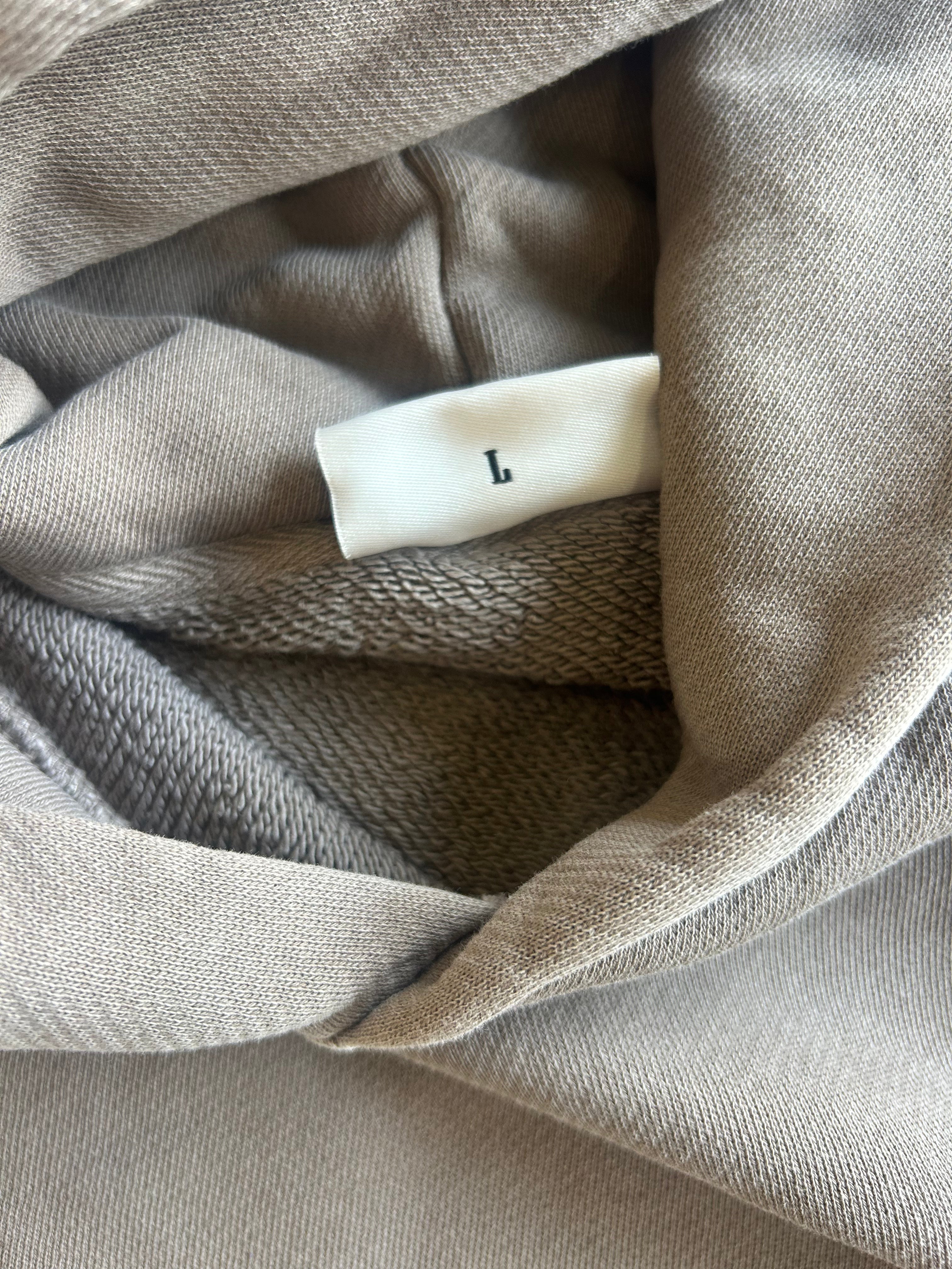 Close-up of a taupe-beige knit garment with a white size tag marked with the letter L