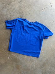 A bright blue short-sleeve crewneck t-shirt laid flat on a textured concrete floor
