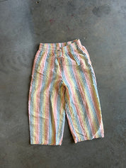 A pair of pastel rainbow-striped cropped pants laid flat on a gray concrete floor