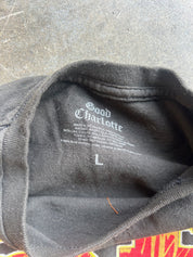 Close-up of the inside collar of a dark charcoal gray t-shirt, showing the printed brand label 'Good Charlotte' and size 'L' on a textured gray concrete floor