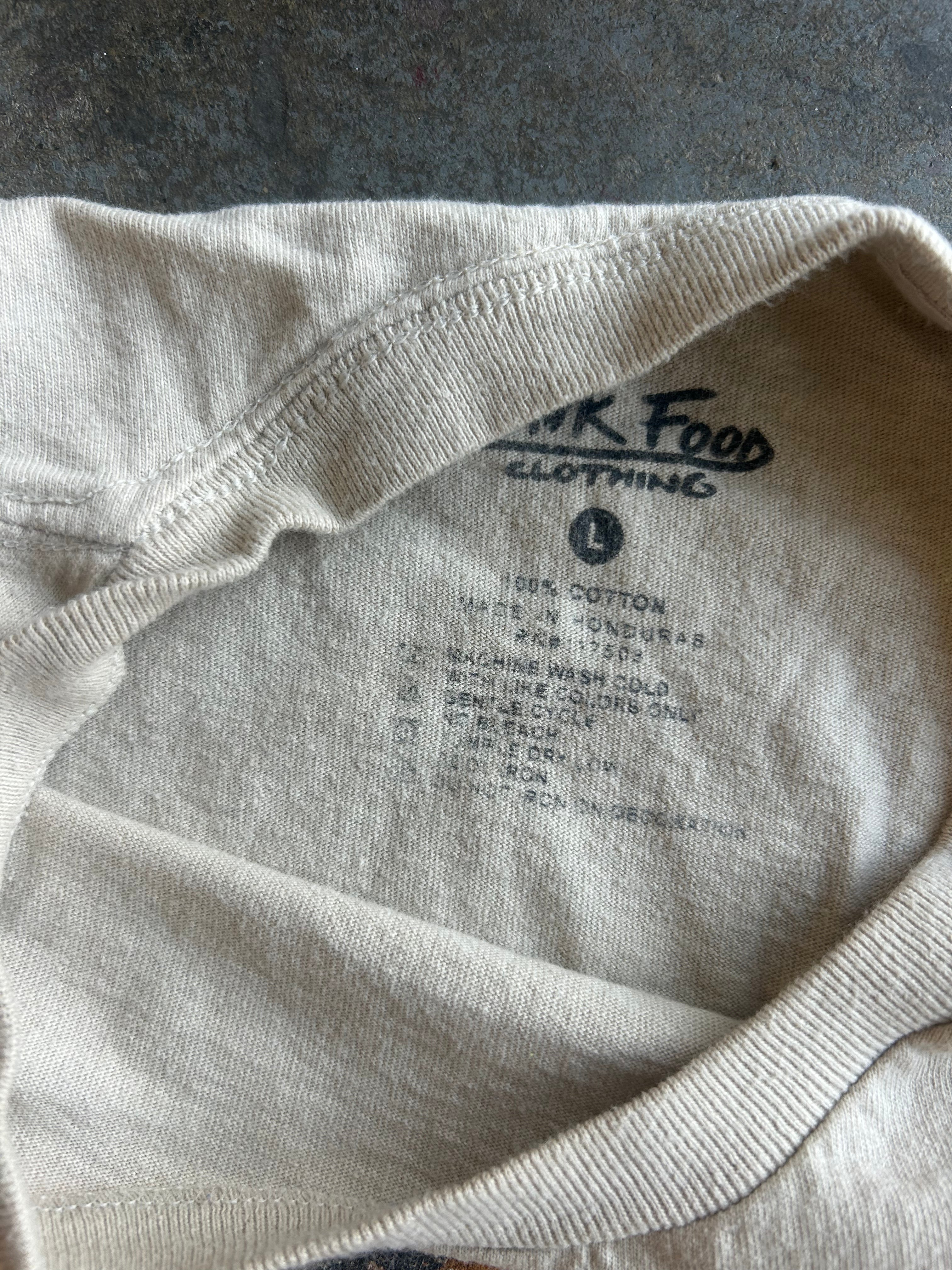 Close-up of the inside collar of a light beige cotton t-shirt, showing the printed brand label 'PINK FOOD CLOTHING' and size information
