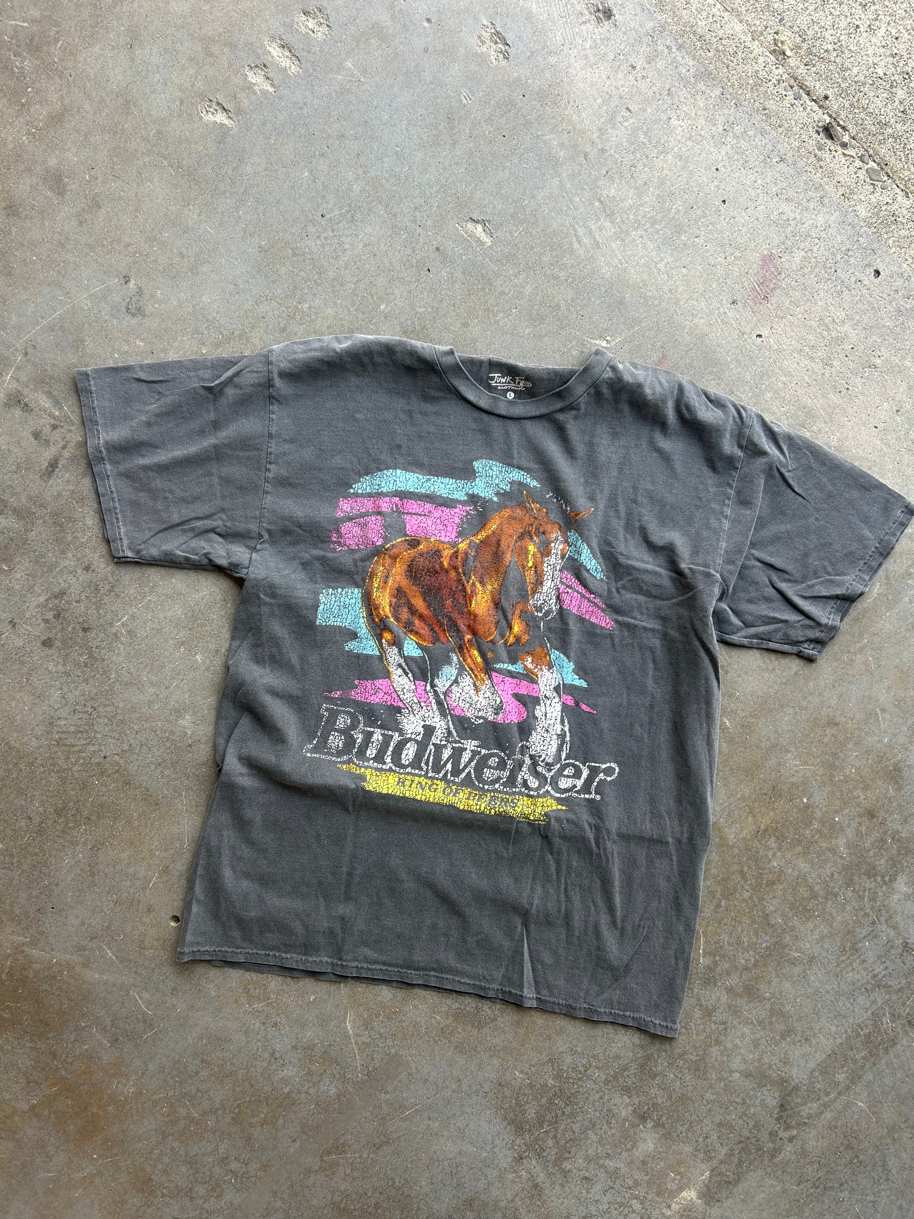 A faded black Budweiser graphic t-shirt featuring a horse design and the Budweiser logo, laid flat on a concrete floor