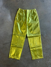Metallic olive green cargo pants with a shiny, crinkled texture, laid flat on a dark gray concrete floor