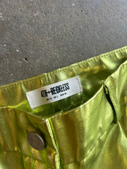 Close-up of metallic olive green pants showing the waistband, white brand label reading 4TH+RECKLESS, and a metal button against a concrete floor