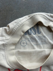 Close-up of the inside neck of a cream-colored t-shirt showing the printed inner collar label with size information and partial brand text