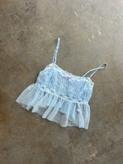 A light blue lace and tulle camisole top with thin spaghetti straps, laid flat on a textured concrete floor
