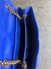 Close-up of a bright blue leather handbag showing the interior lining and gold-tone chain strap against a concrete floor background