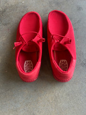 A pair of red slip-on shoes with tassel laces, photographed from above on a gray concrete floor. The brand name 'Hex Dude' is visible on the insoles